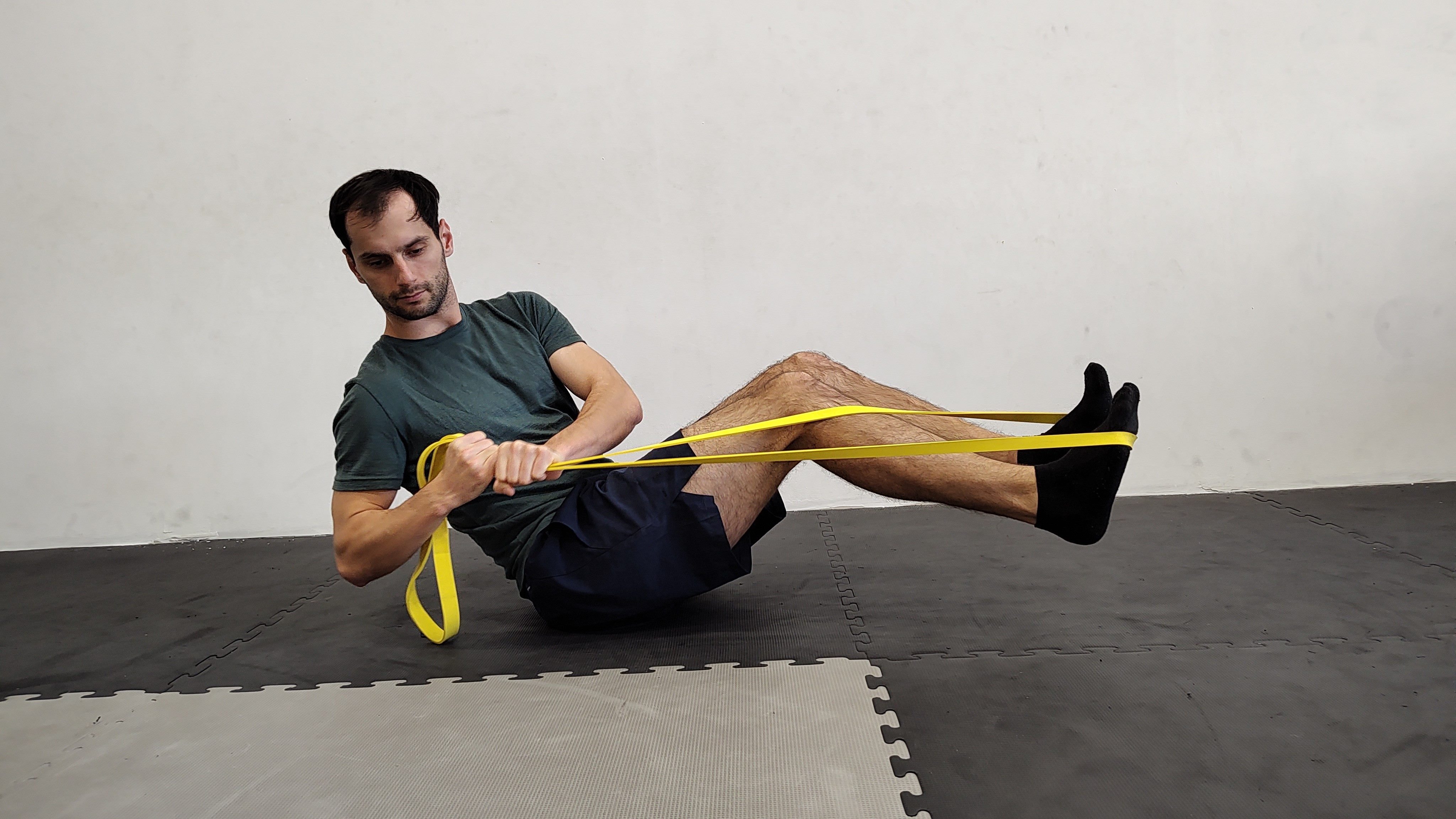 Muž v tělocvičně cvičí ruský twist s nohama nad podložkou s expandérem.